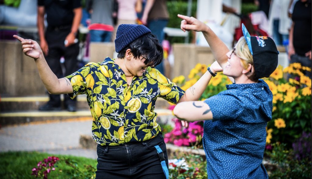 Two people very much enjoying the music of Burnaby Pride, dancing on the grass, arms waving in the air.
