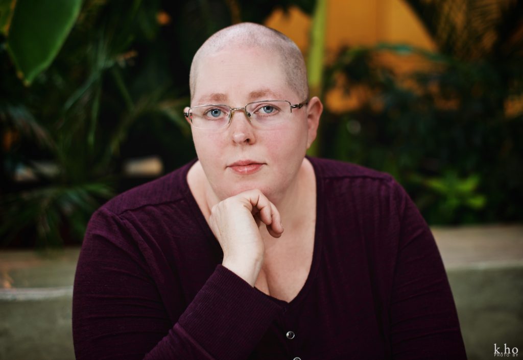 Heather in red shirt, sitting in front of green plants, head resting on open fist